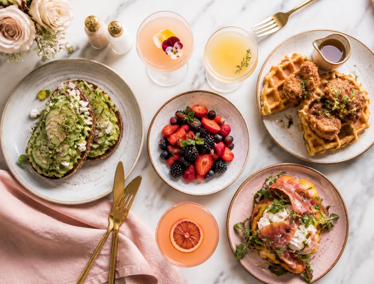 Brunch spread with avocado toast, chicken and waffles, berries and cocktails on marble